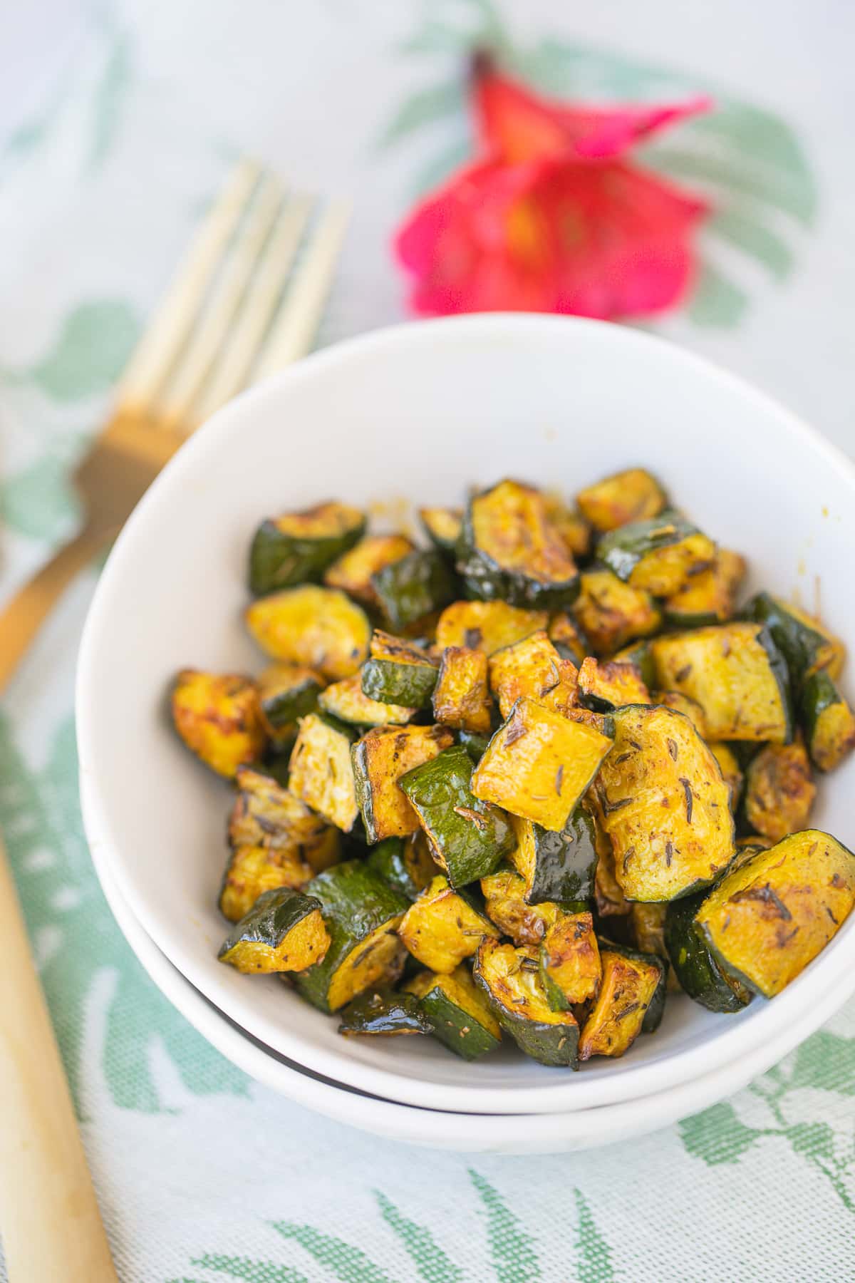 red palm oil roasted zucchini in a white bowl with gold forks
