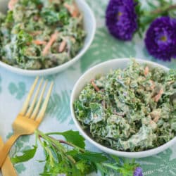 two bowls of kale salad with gold forks and purple flowers