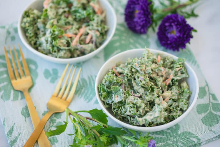 two bowls of kale salad with gold forks and purple flowers
