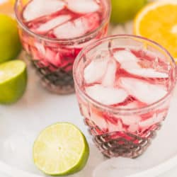 two glasses of tart cherry mocktail on a platter with fresh citrus fruit