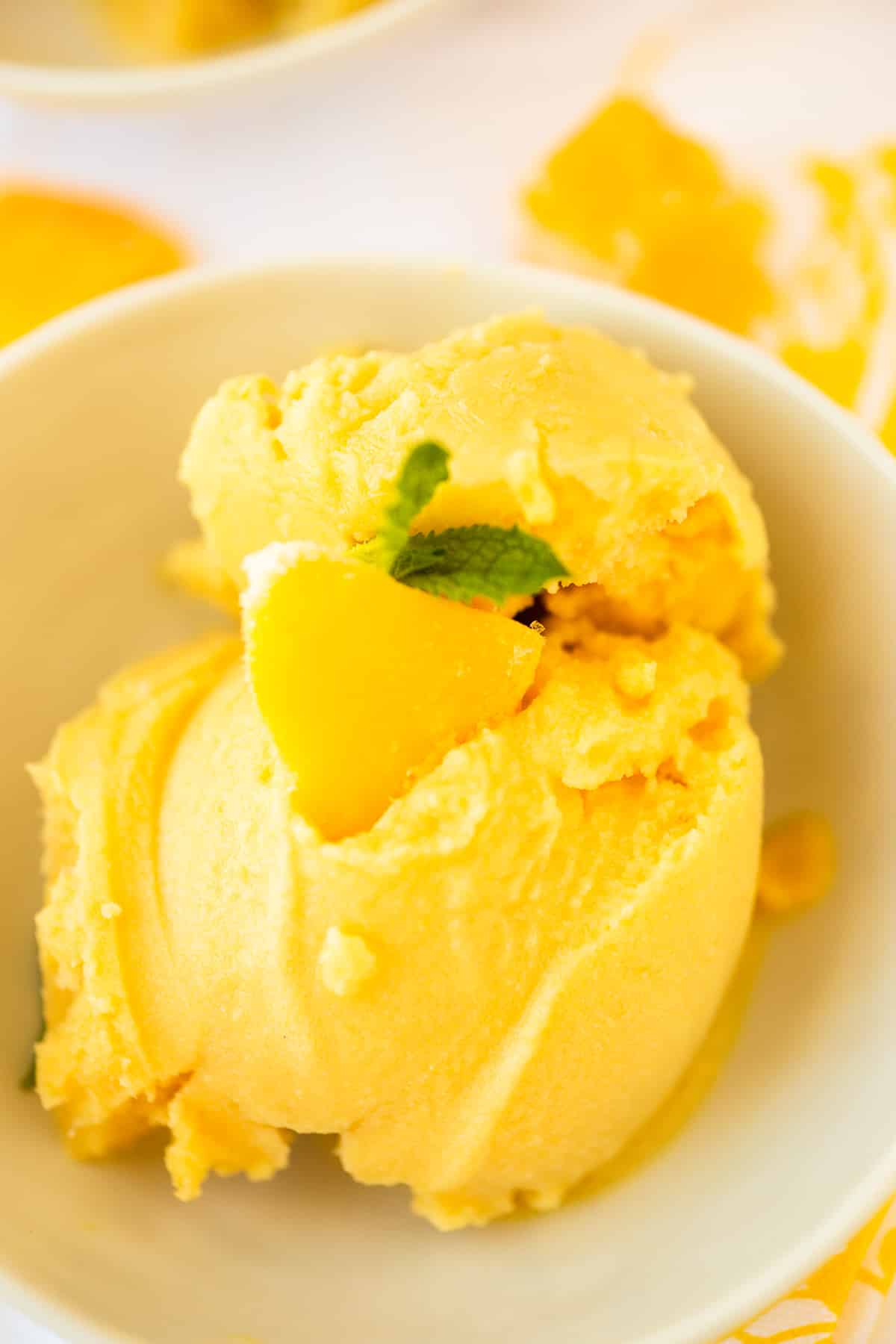 two scoops of mango ice cream in a bowl topped with fresh mint leaves