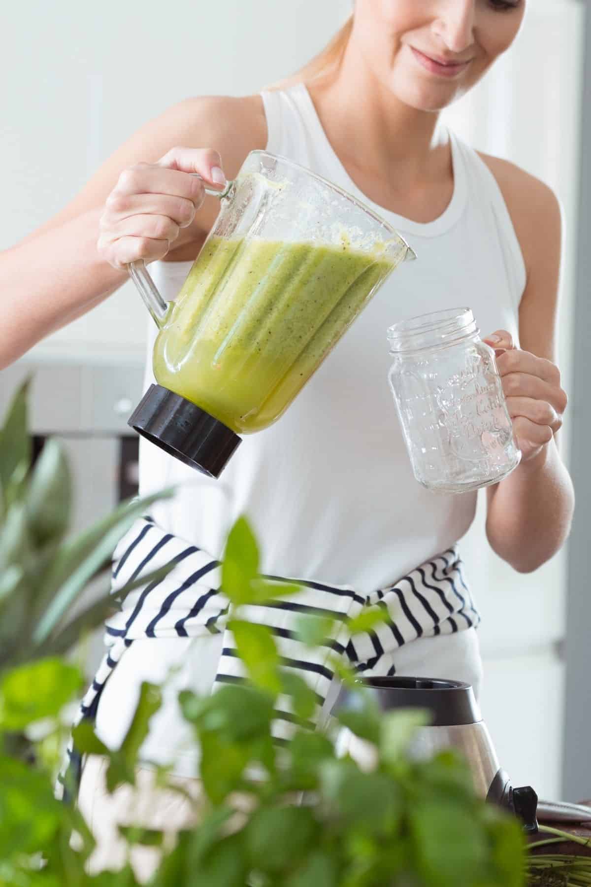 woman pouring a green smoothie from blender into glass.