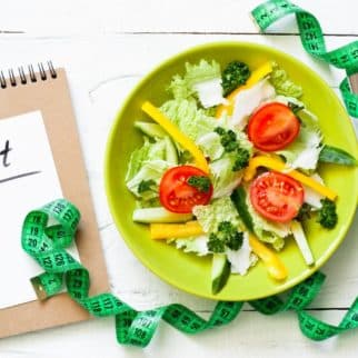 diet notebook on a table with a salad and a measuring tape