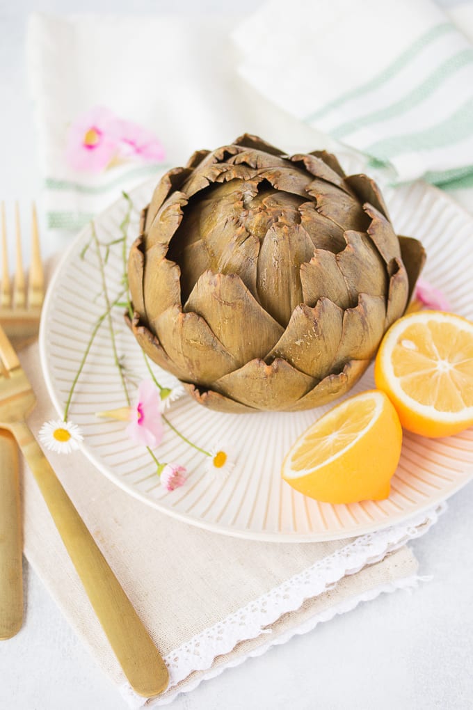 cooked artichoke on a plate with fresh lemon