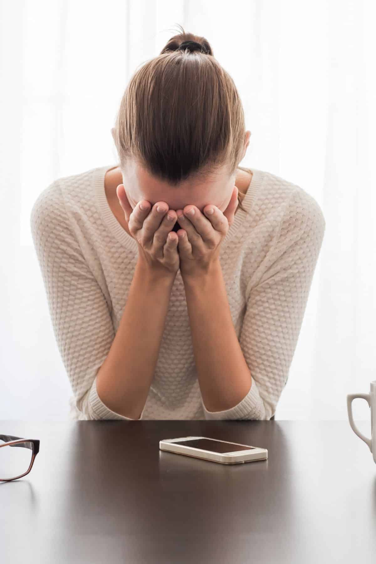 woman sitting at table holding her head in hands.