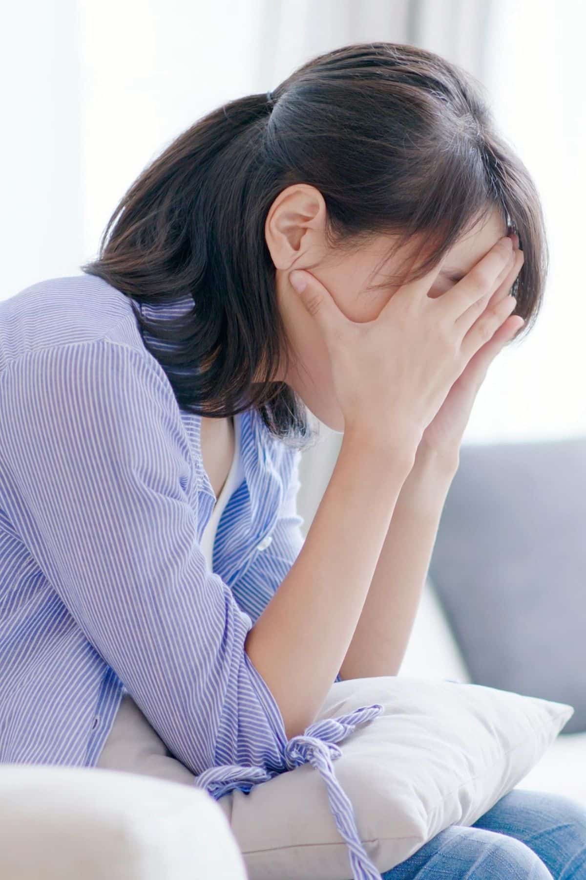 depressed woman sitting on coach with hands covering her face.