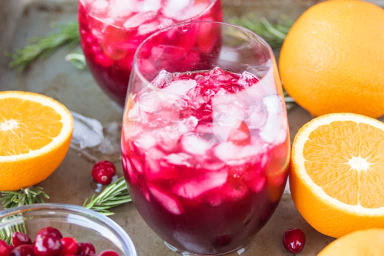 two glasses of pomegranate cranberry mocktail served with fresh orange slices