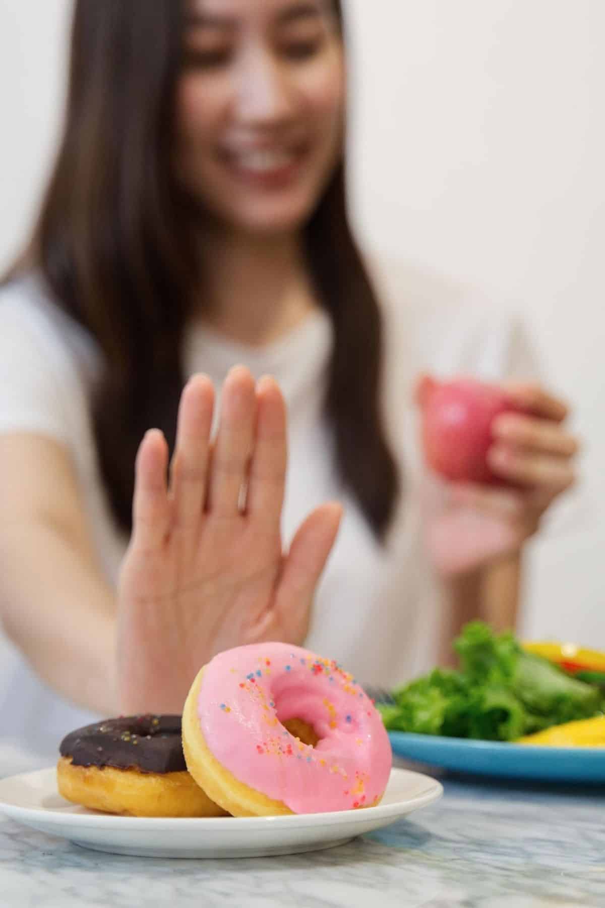 woman pushing away a donut in favor of healthier foods