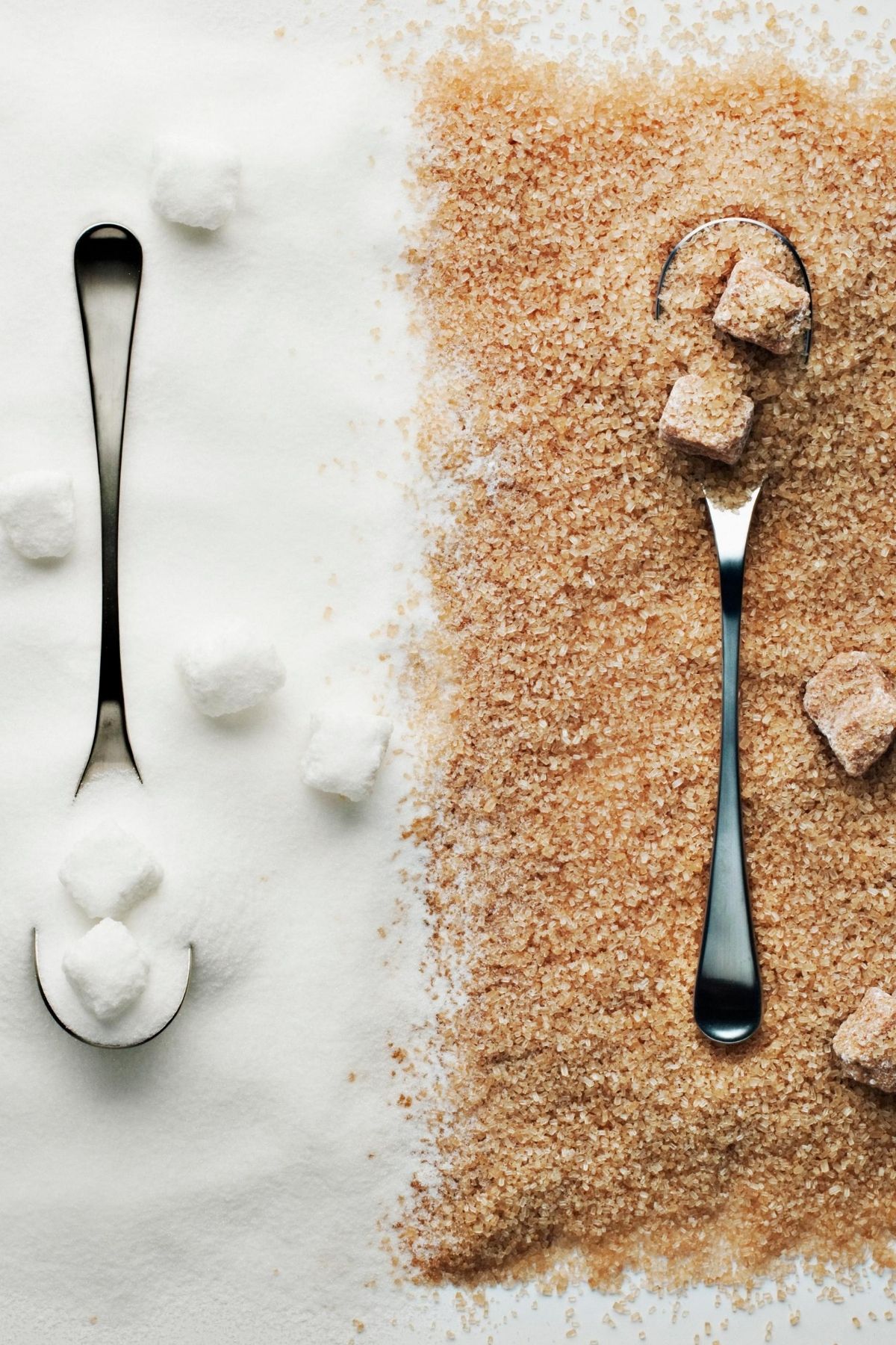 two spoons on a counter with white sugar and brown sugar.