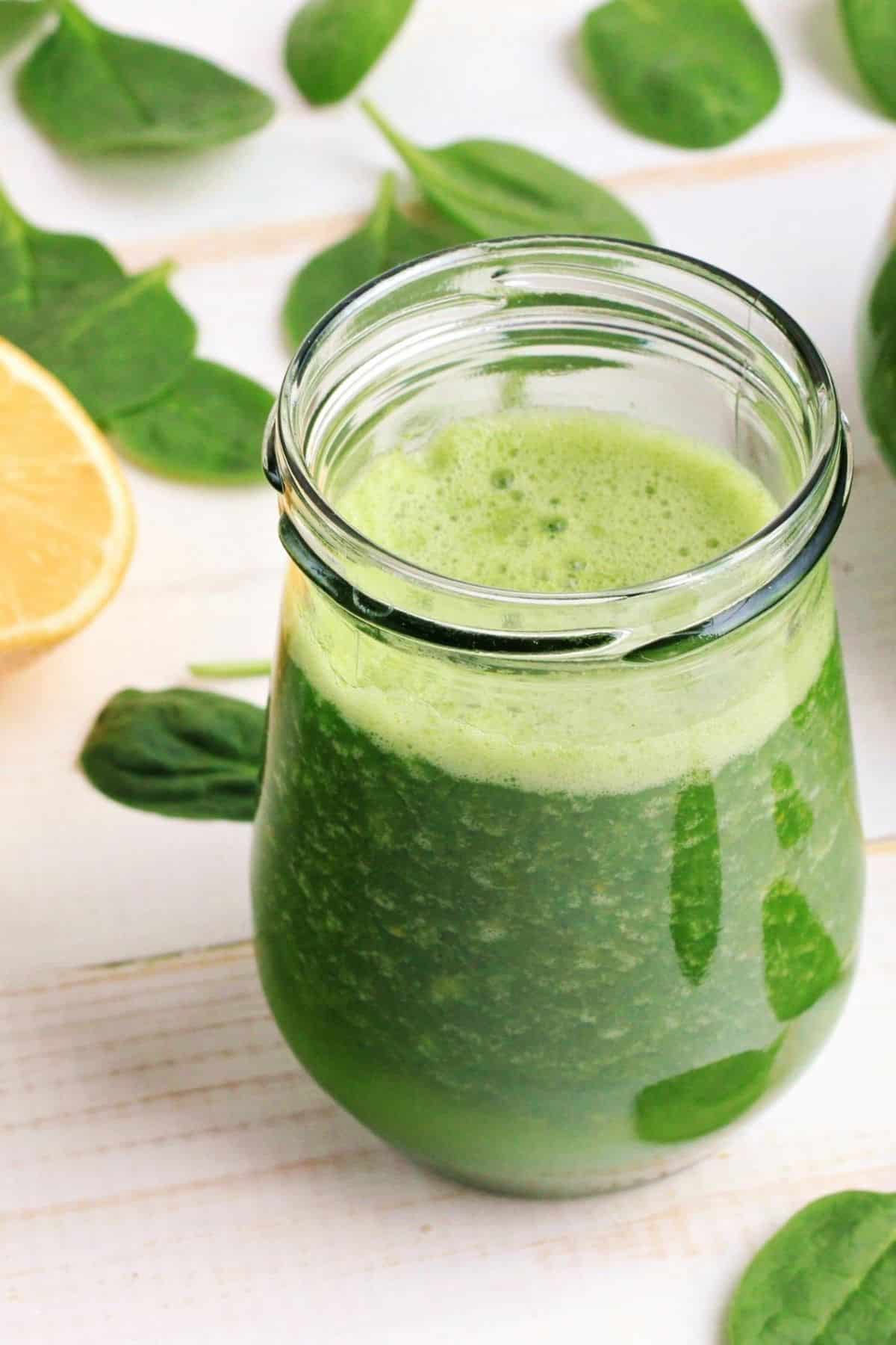 green juice in a glass with fresh spinach and a lemon in the background