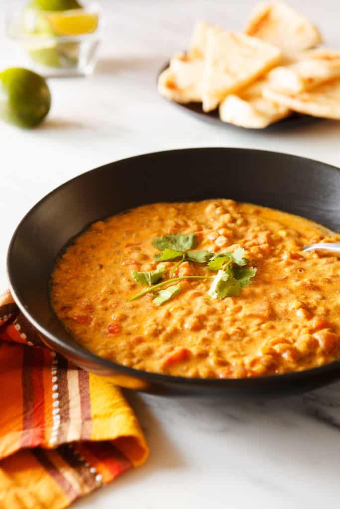 Creamy orange lentils in a bowl with flatbread and citrus in the background.
