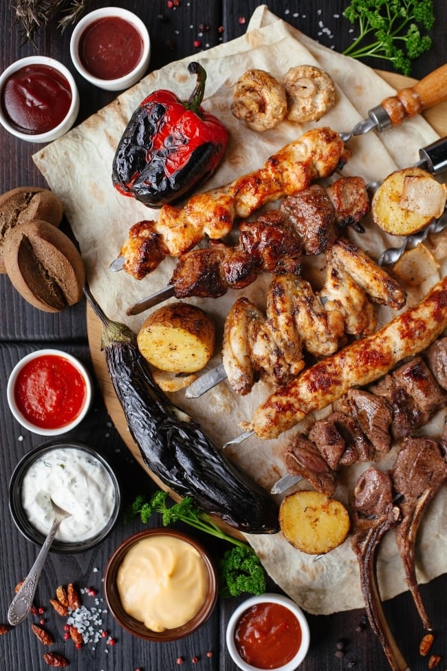 Pork and chicken skewers on a platter with dipping sauces