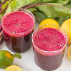 two glasses of homemade beet juice surrounded by lemons and beet greens