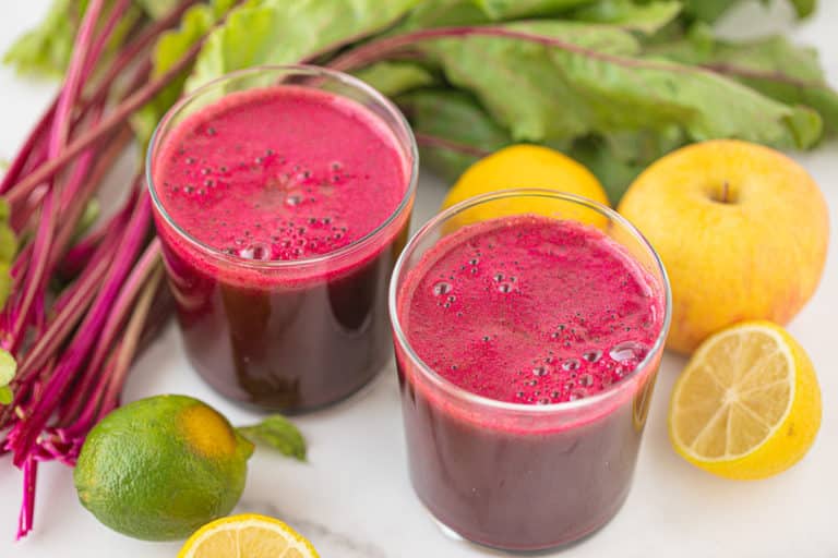 two glasses of homemade beet juice surrounded by lemons and beet greens.