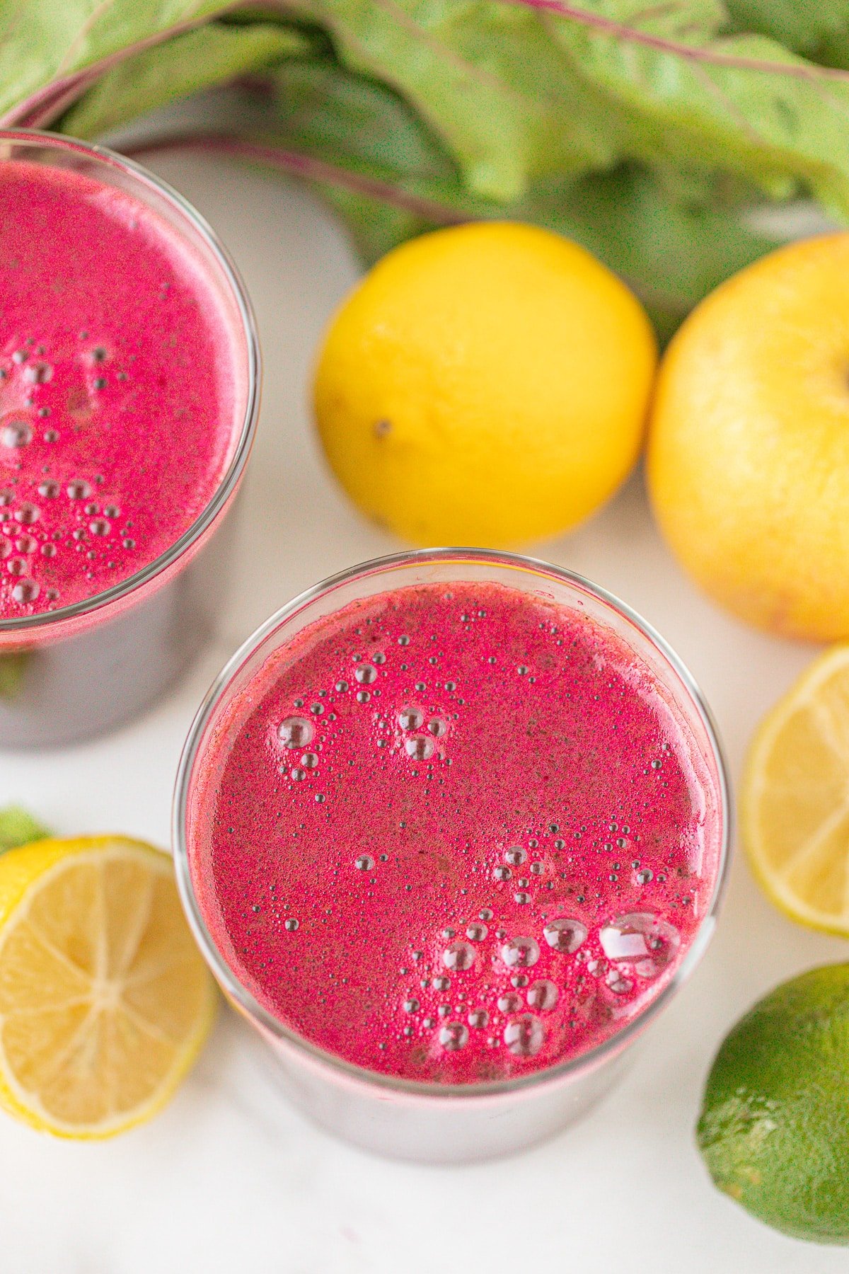 two glasses of fresh beetroot juice on a countertop with fresh lemons