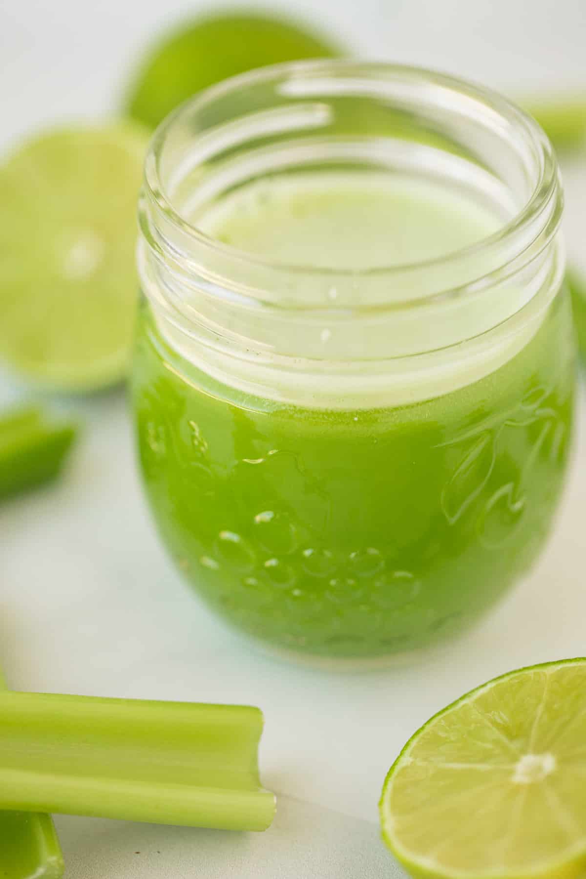 glass of celery juice on a table with celery and limes.