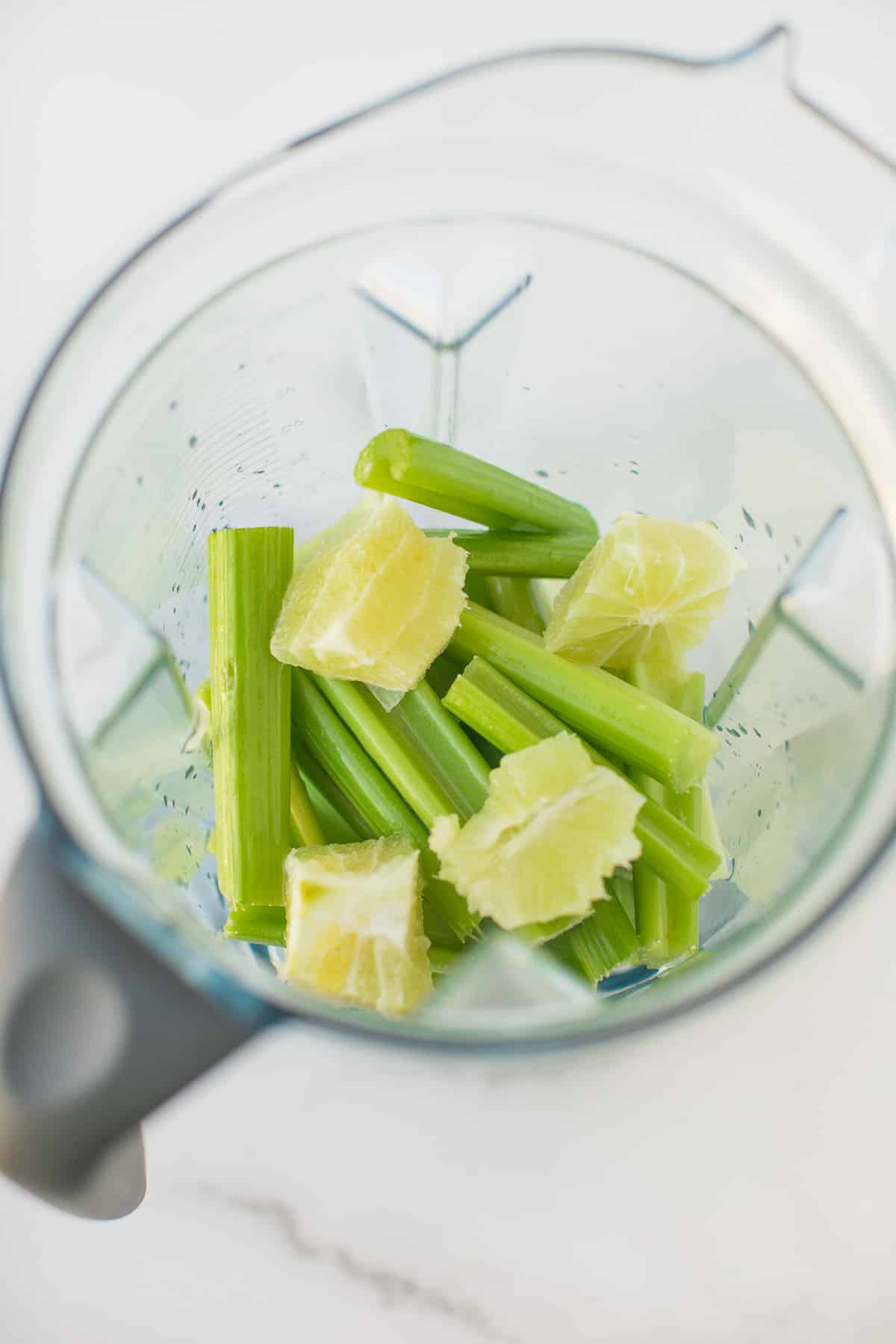 celery stalks and peeled limes in the base of a vitamix