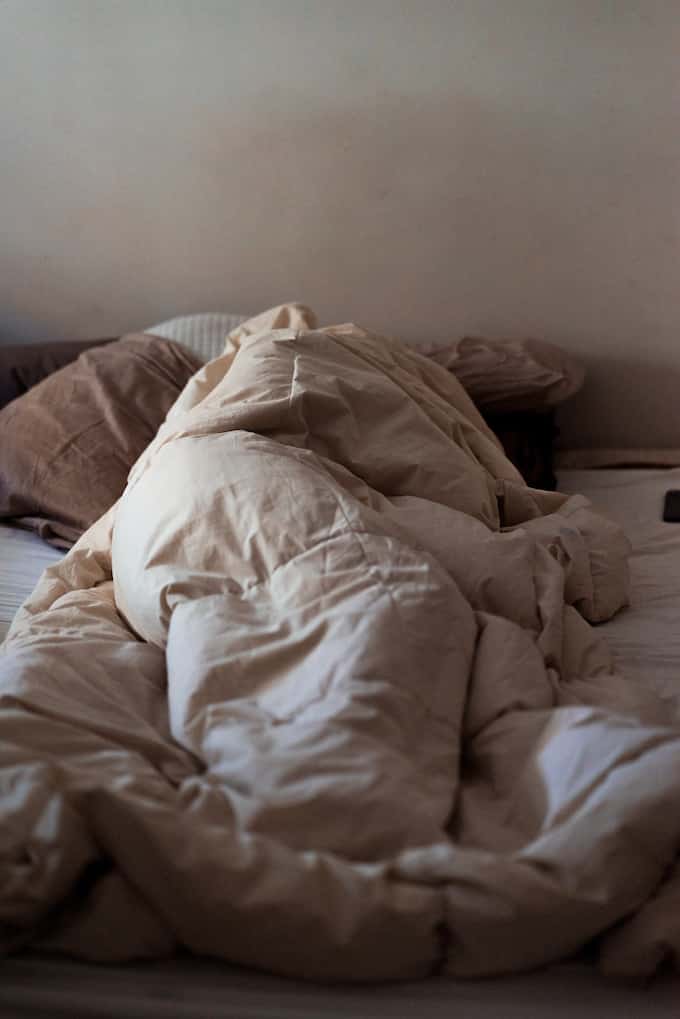 tired person sleeping in bed with comforter.
