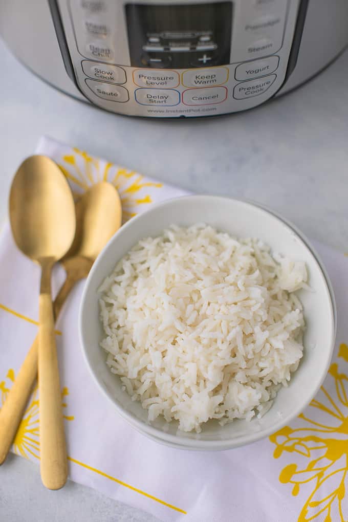 cooked rice in a white bowl with two gold spoons