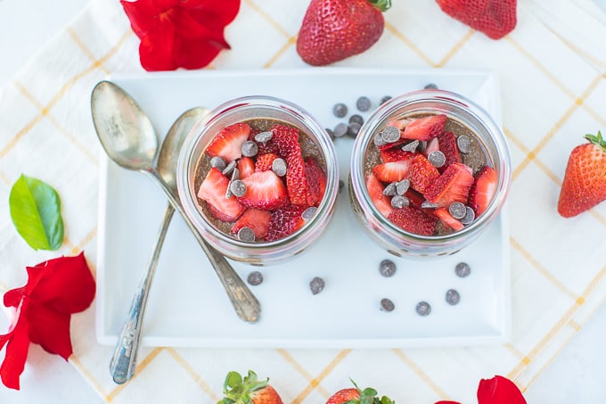 two jars of chia pudding on a white platter with spoons for serving