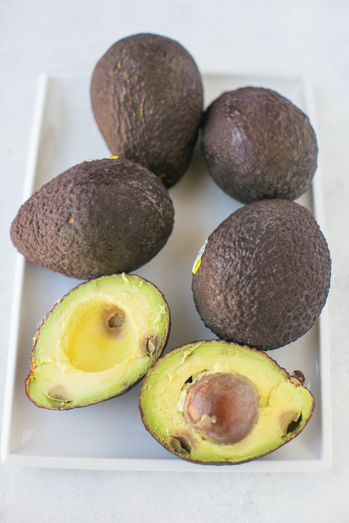 avocados on a white platter with one cut in half.