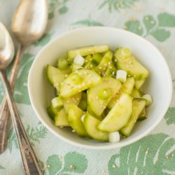 cucumber salad in a white bowl with two spoons