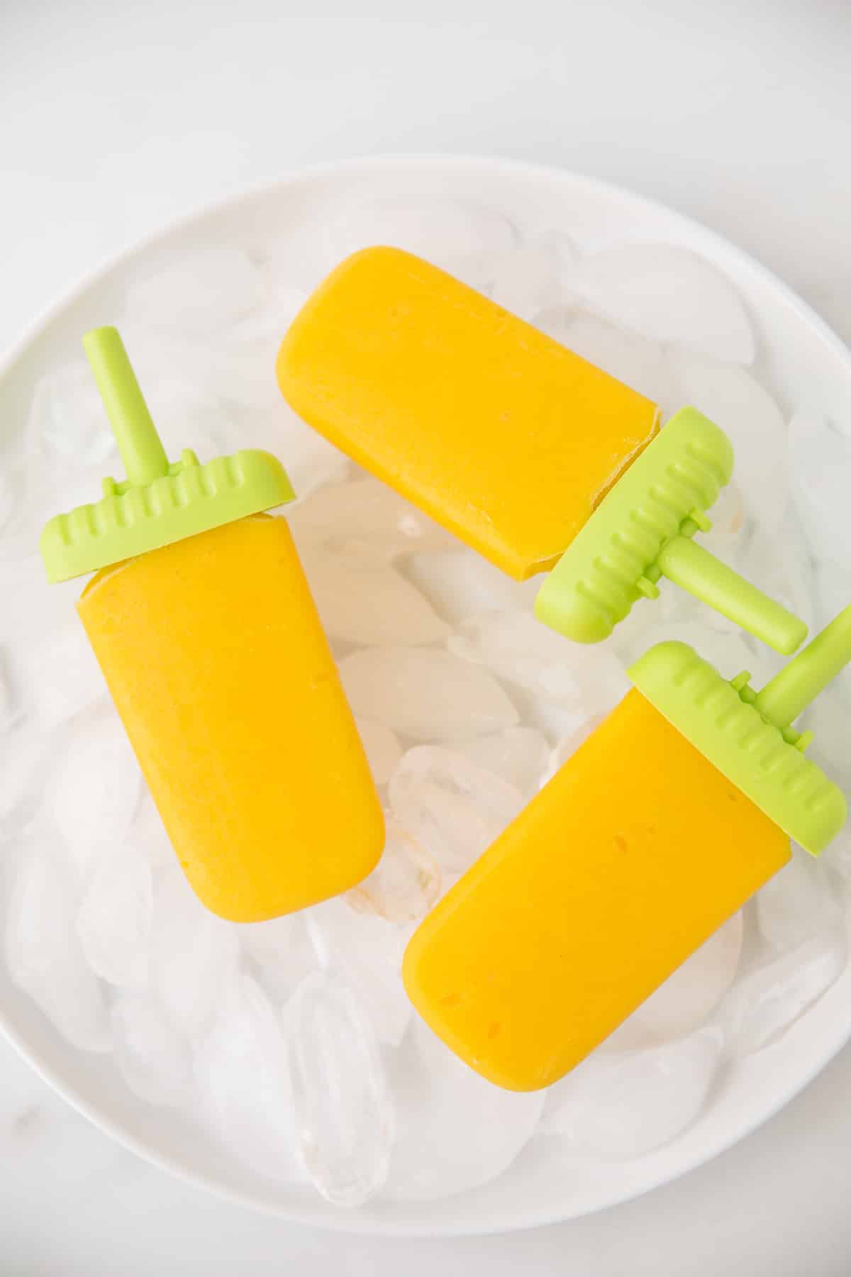mango pineapple popsicles in a bowl with ice