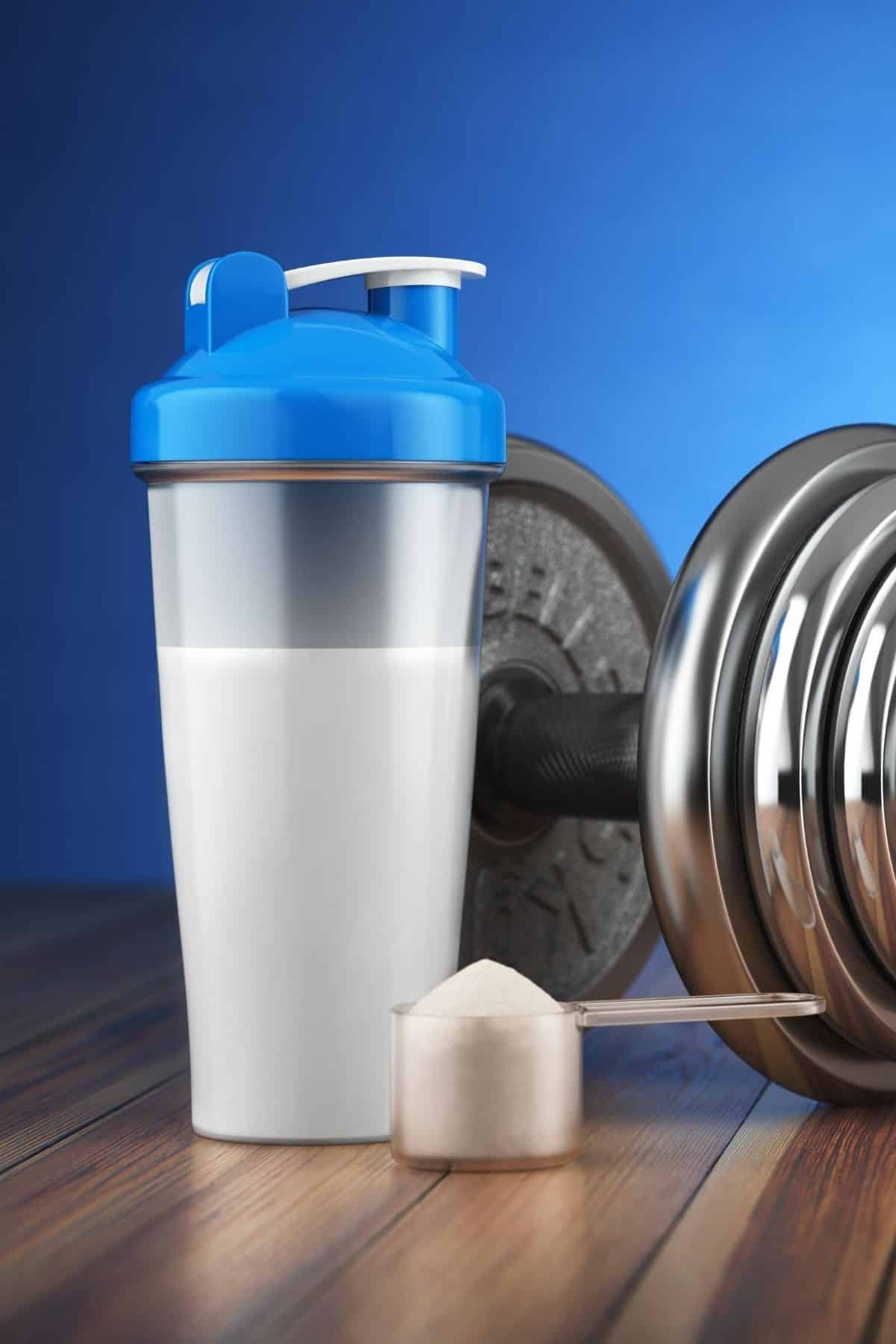 shaker bottle with a scoop of protein powder next to a dumbbell for working out.