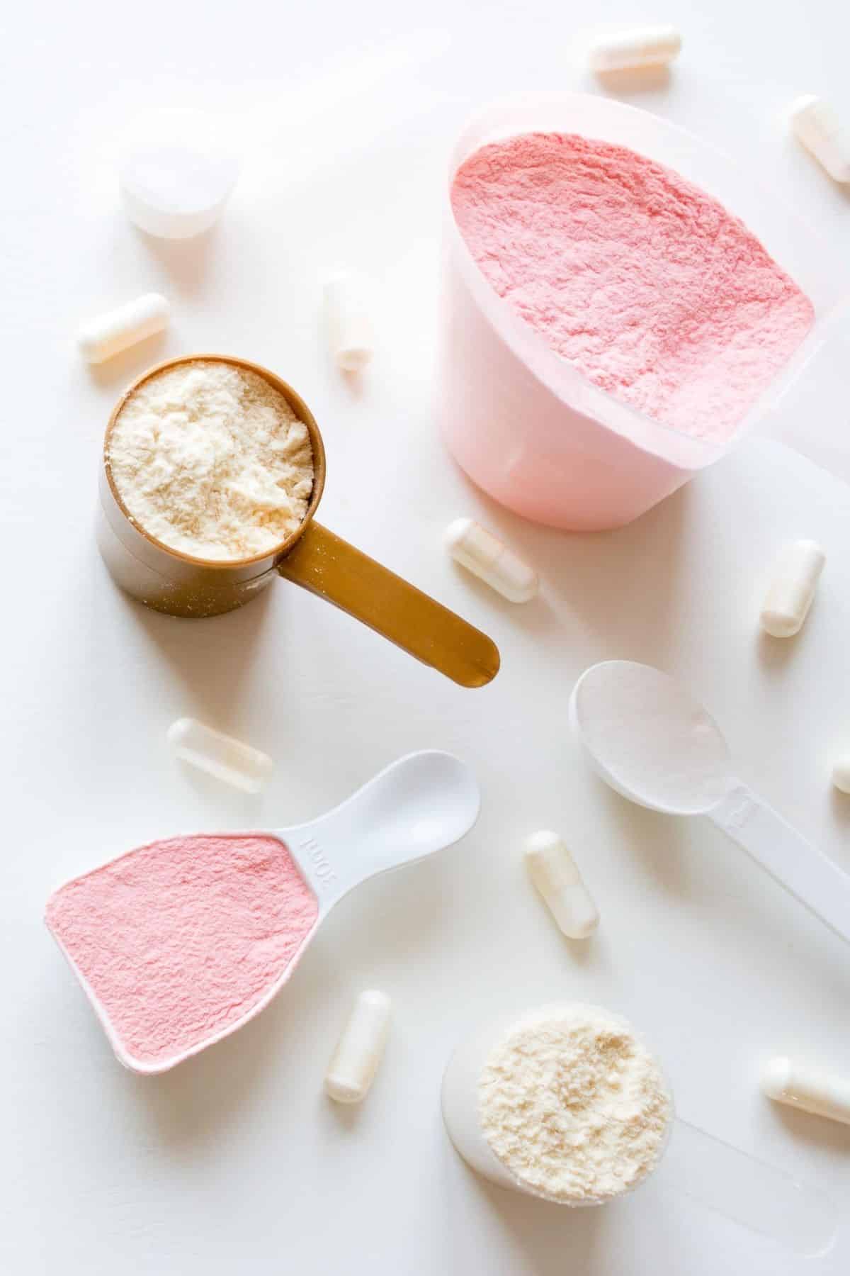 bowls of pink and white powders with some white capsules on a countertop