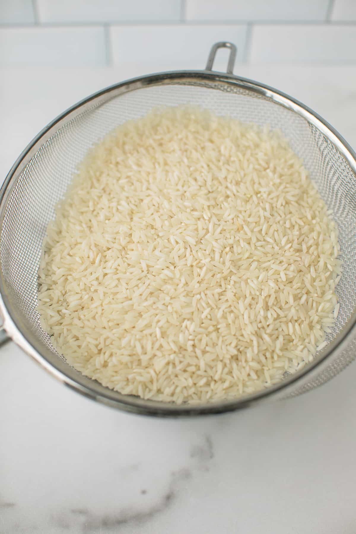 white rice in a fine mesh colander for rinsing.