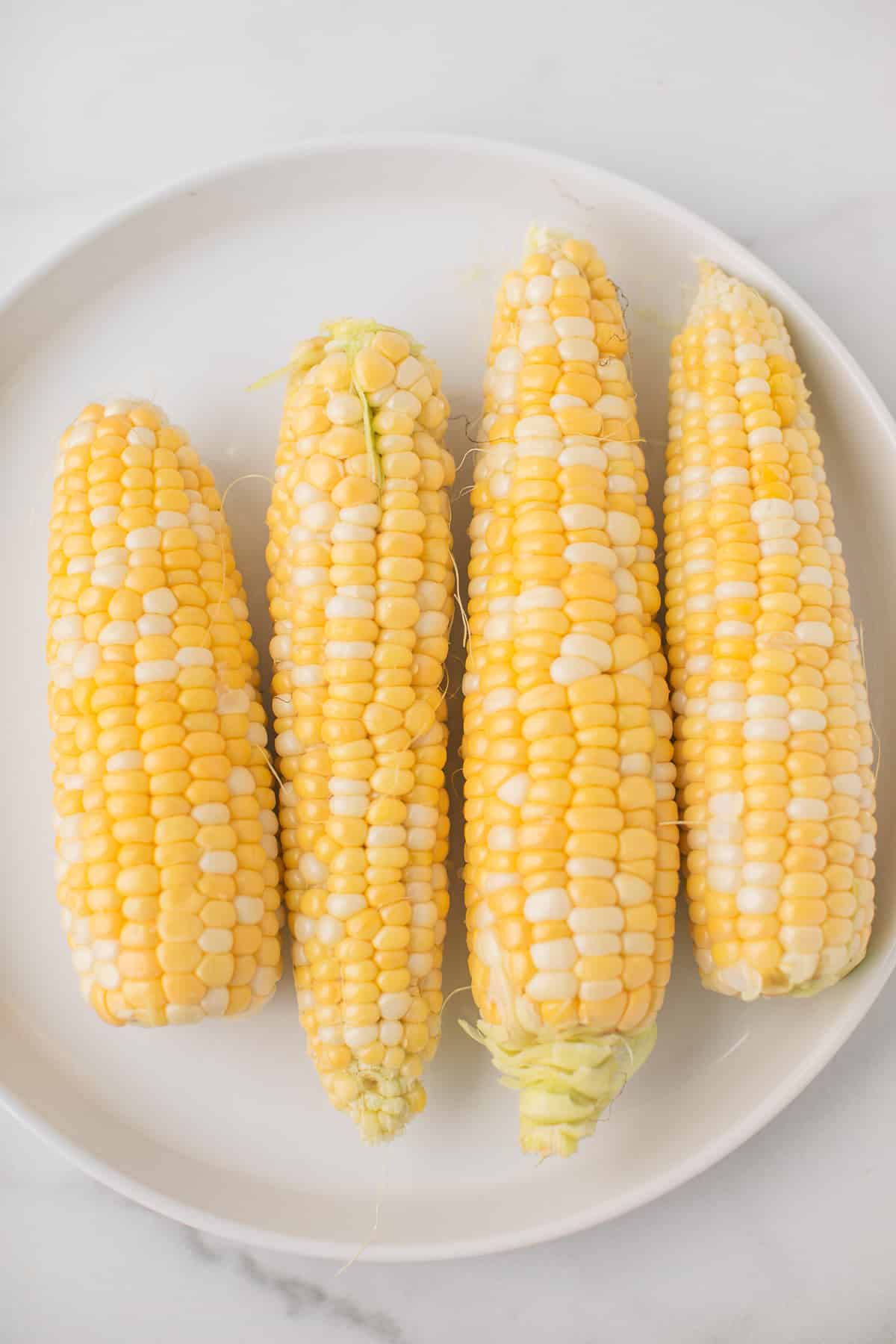 four pieces of corn on a plate with the corn husks removed