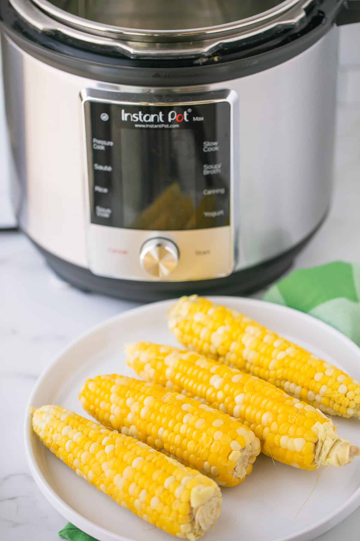 plate of cooked corn on the cob in front of an instant pot pressure cooker
