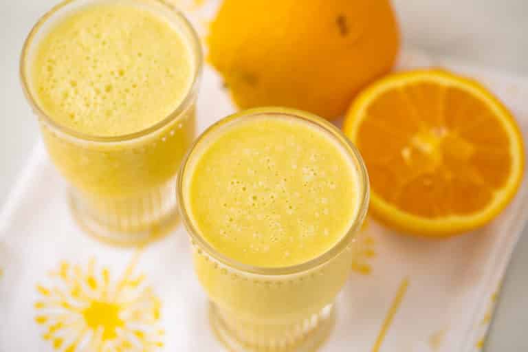 two glasses yellow smoothie with oranges