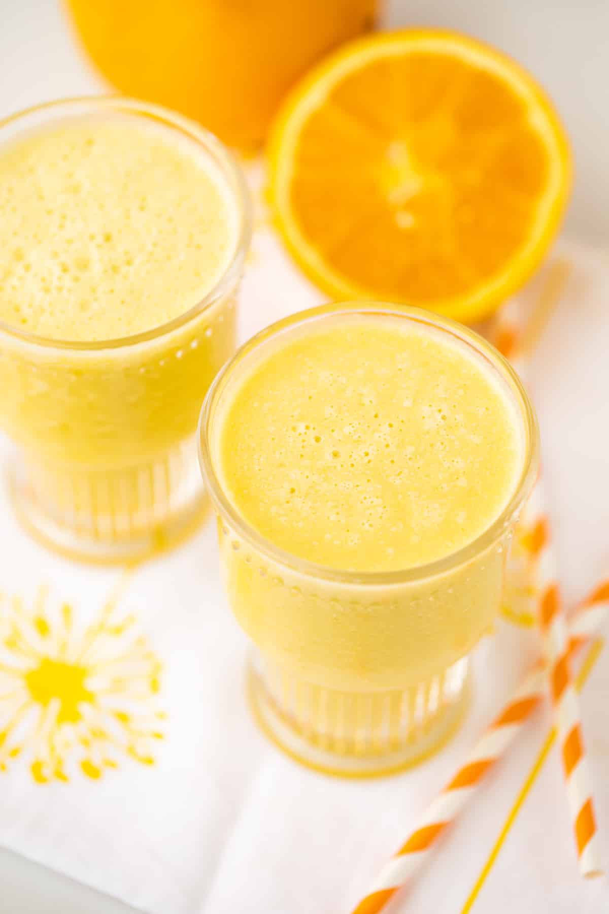 two glasses of pineapple orange smoothie with sliced oranges.