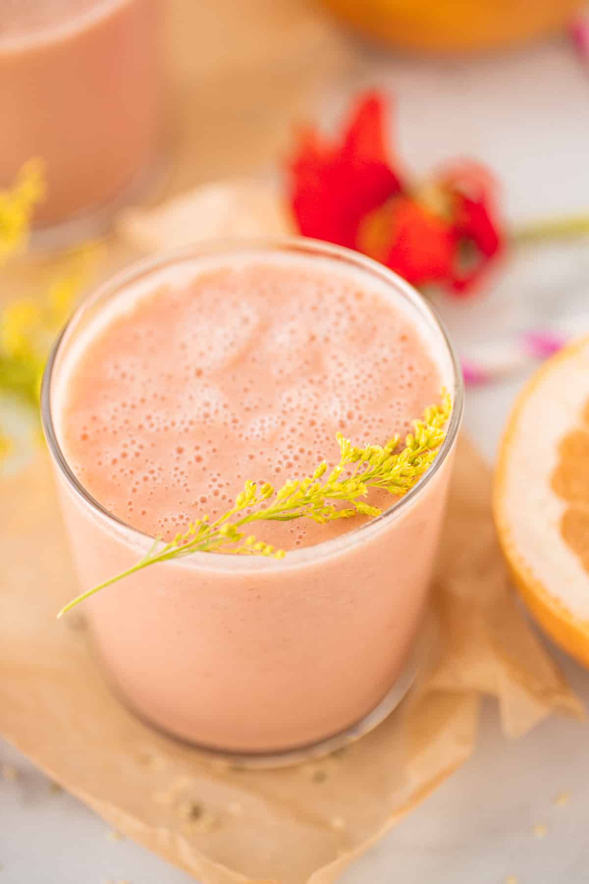 glass of grapefruit smoothie with a sprig of yellow flowers on top of the glass
