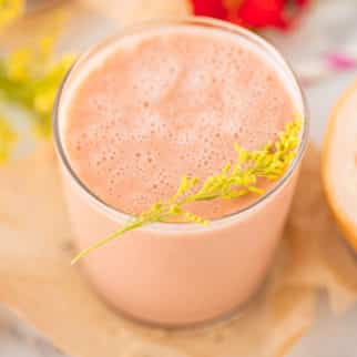 glass of pink smoothie with fresh flowers in the background