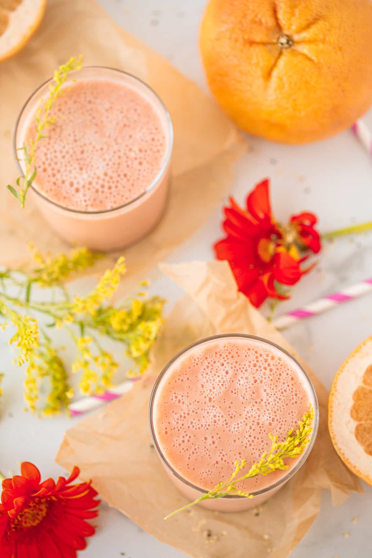 two glasses of pink smoothie on a background with fresh flowers and striped straws.