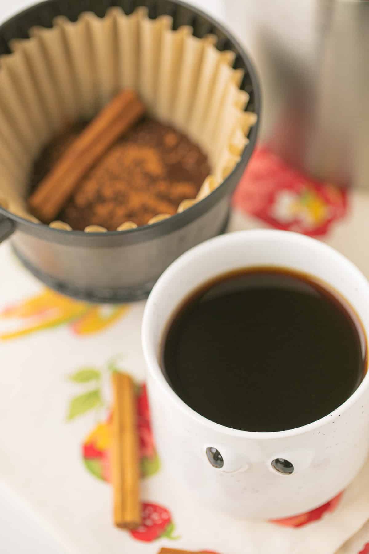 pumpkin spice coffee in a white mug next to cinnamon sticks.