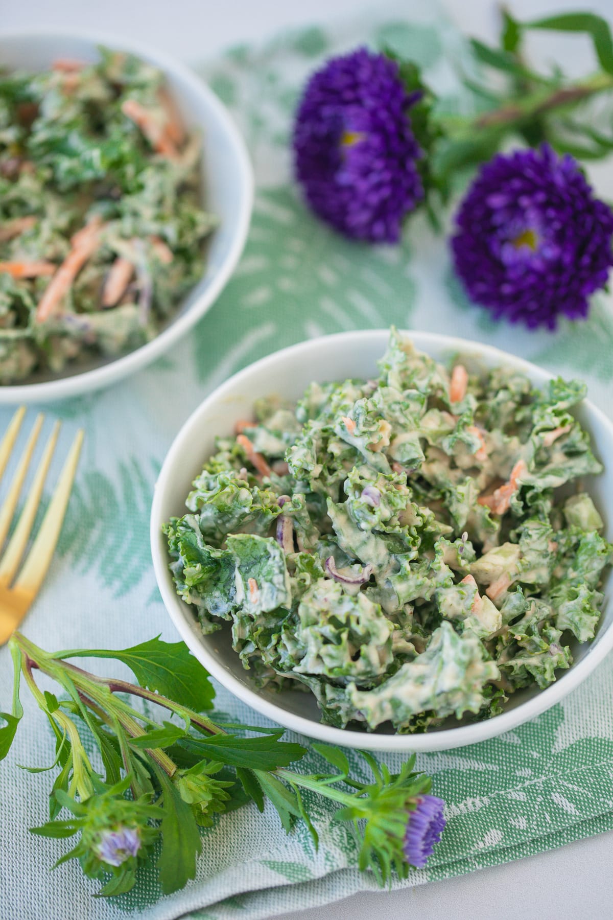 bowl of kale salad on a green floral napkin with fresh purple flowers.
