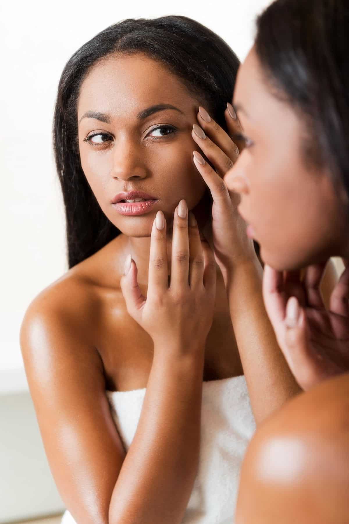 young woman looking at her skin in a mirror.