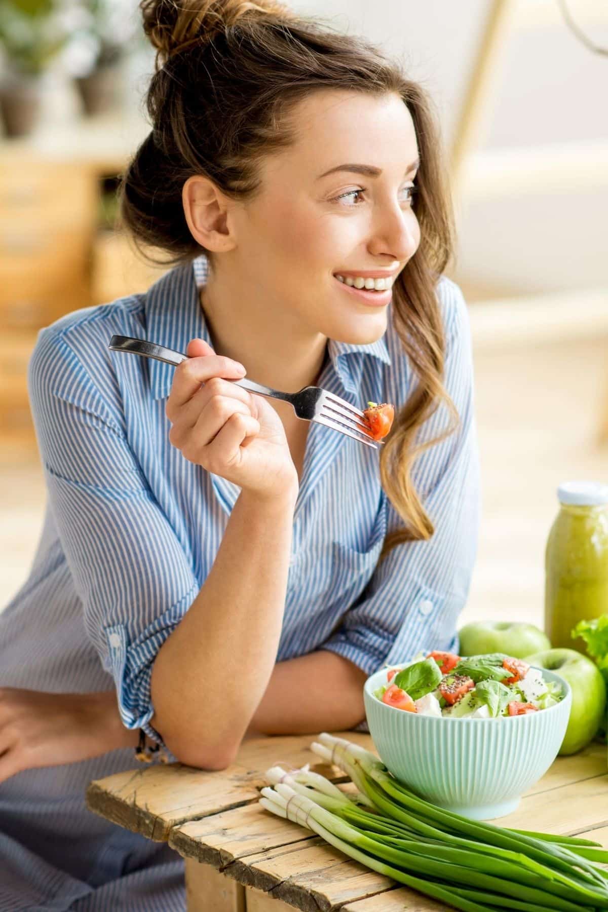 woman smiling while she's eating a salad.