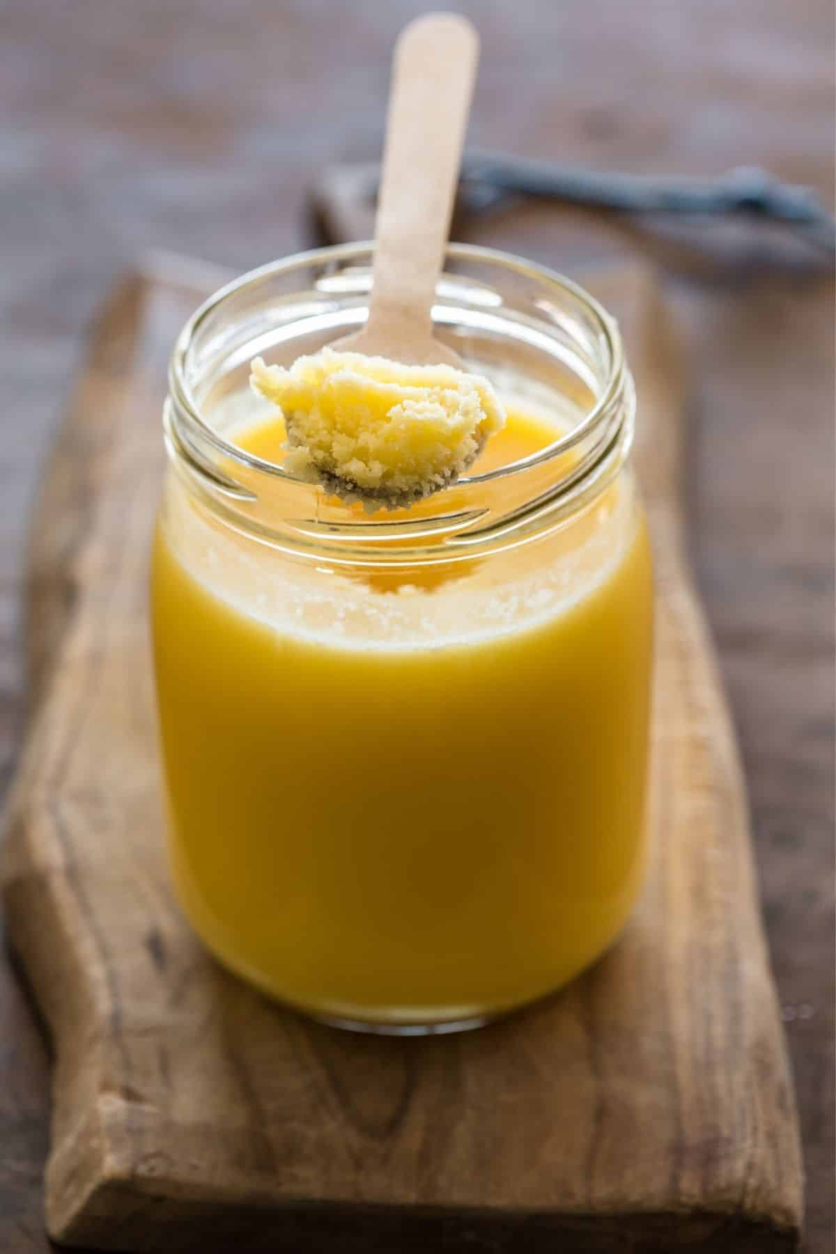 jar of ghee on a wood countertop with a wooden spoon 