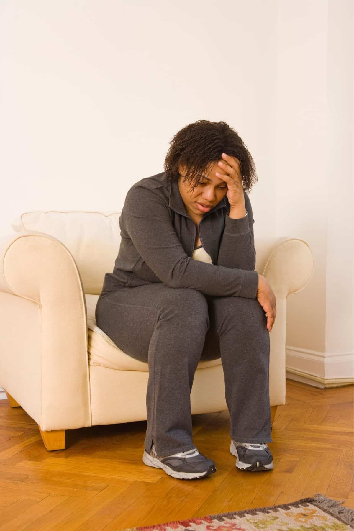 tired woman sitting on a chair holding her head.