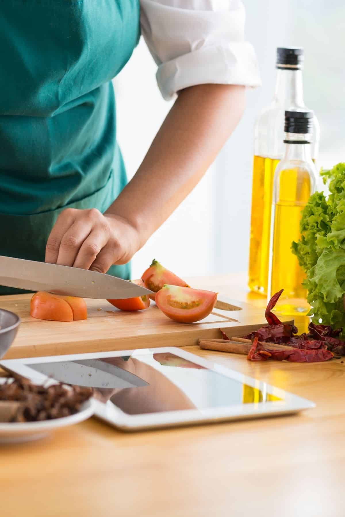 woman chopping a tomato while looking at a recipe on an iPad