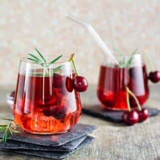 cherry mocktail on table garnished with cherries and rosemary.