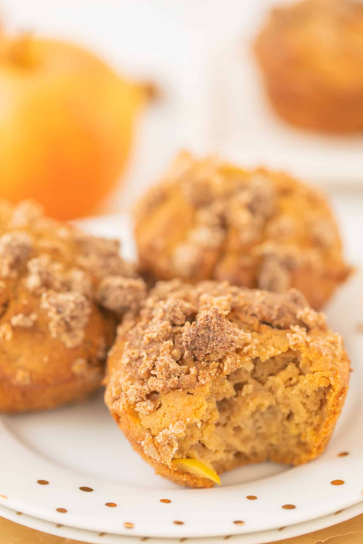 three apple muffins on a plate with a bite taken out of one