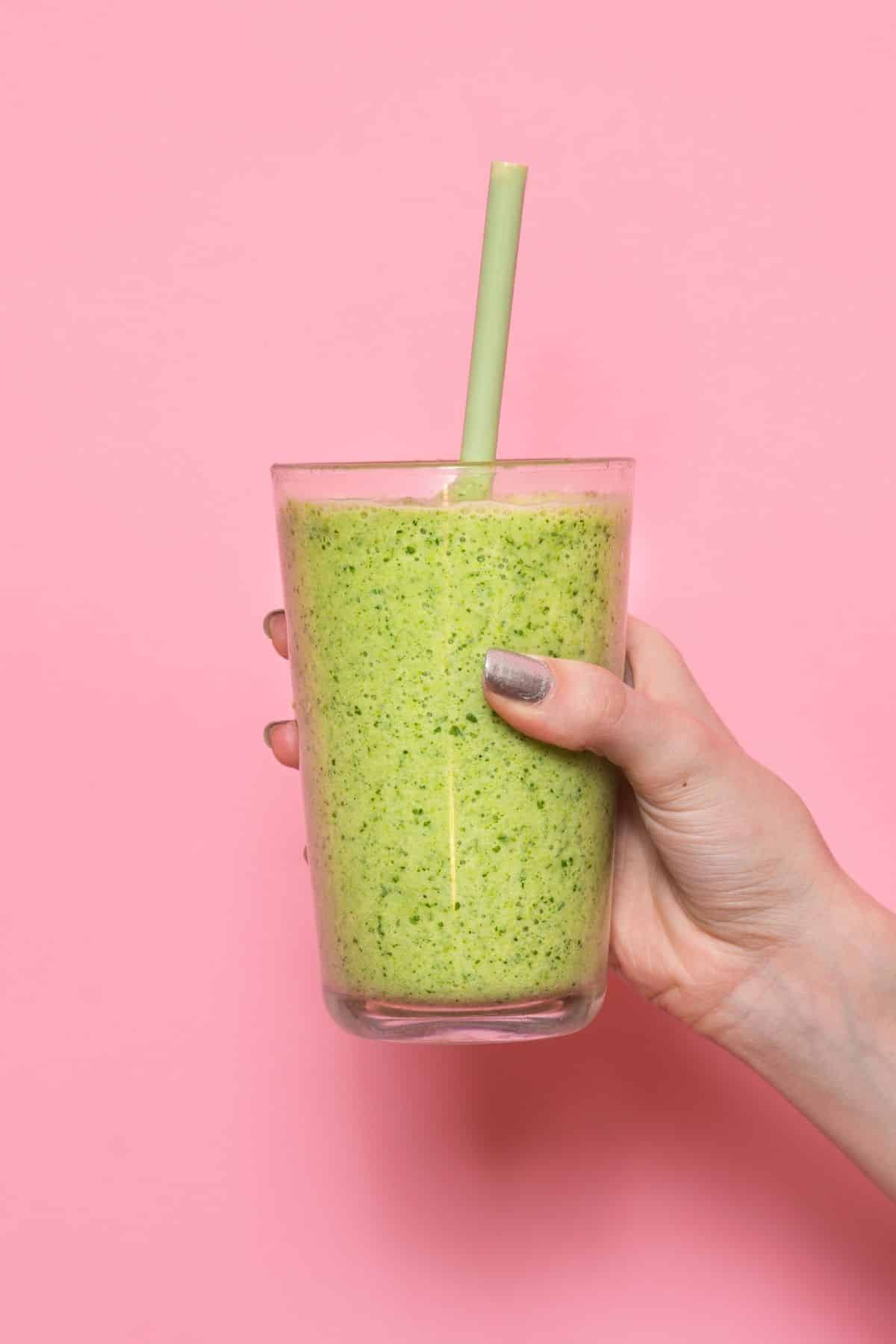 woman holding a green smoothie in front of a pink background