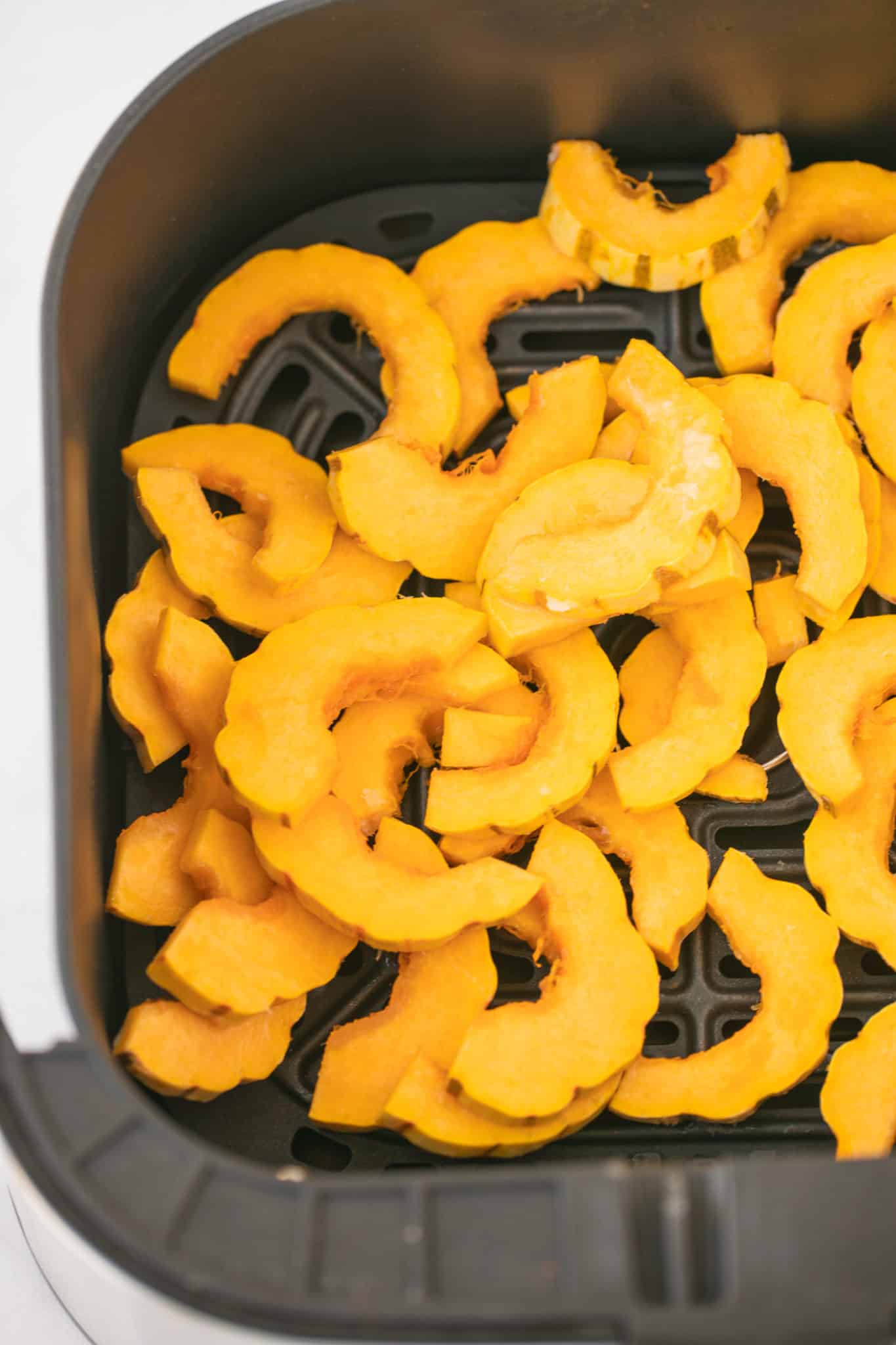 sliced Delicata squash in the basket of an air fryer.