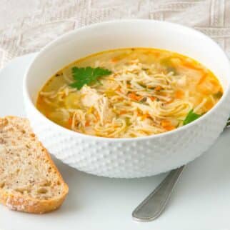 bowl of instant pot chicken noodle soup on plate with bread.
