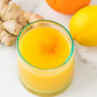 juice served in a glass on a table with fresh ginger, lemon, and orange